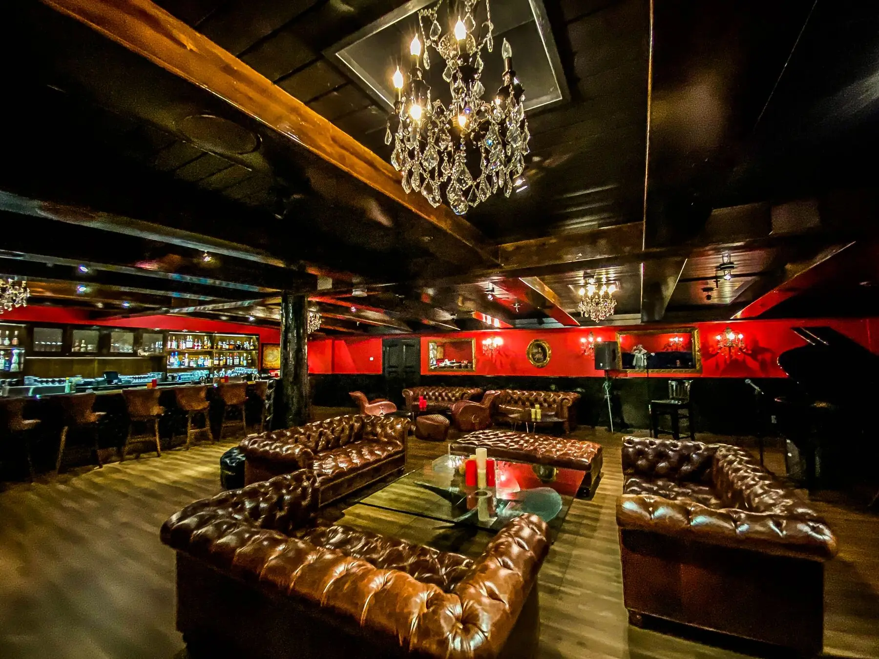 Inside the Killer Yacht Club speakeasy in Marina del Rey: tufted leather sofas, a crystal chandelier, red walls, a full bar, and a grand piano and stage for live music